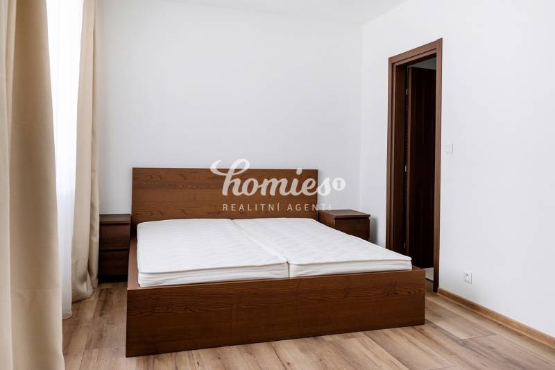 Hálószoba egy háromszobás lakásban sötét fa ággyal és fa dekorációjú padlóval.