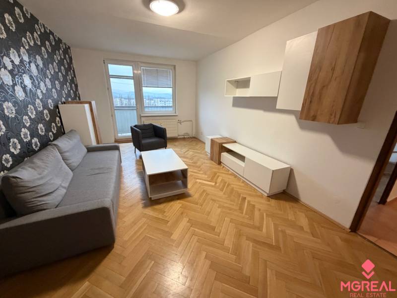 Nappali egy háromszobás lakásban szürke ülőgarnitúrával és virágos tapétával a falon.