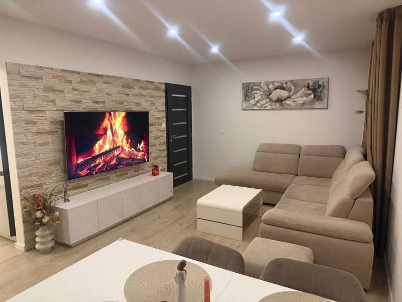 Nappali egy háromszobás lakásban sarokkanapéval és fa mintázatú padlóval.