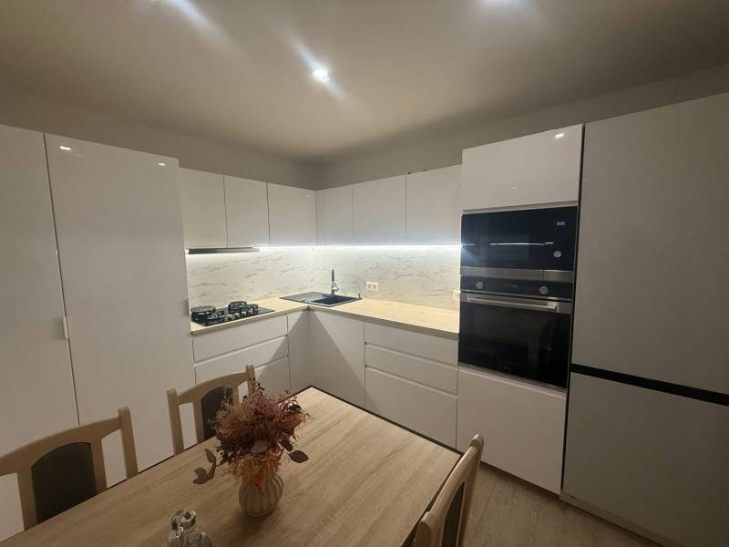 Modern konyha egy háromszobás lakásban fehér szekrényekkel és márvány burkolattal.