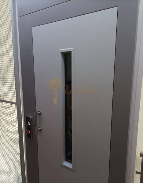 Szürke ajtó üvegkémlelővel és liftgombbal, fotó egy egyszobás lakásban.