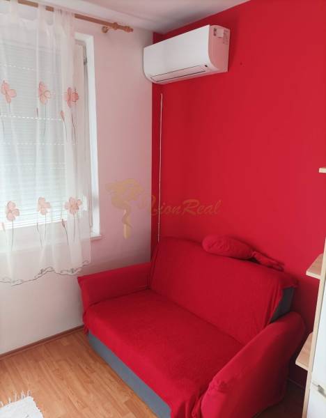 Piros kanapé, fali légkondicionáló és függöny egy egyszobás lakásban, fa dekor padlóval.