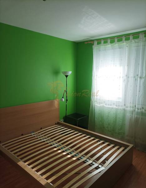 Hálószoba egy egyszobás lakásban ággyal, zöld falakkal és fa dekorációjú padlóval.