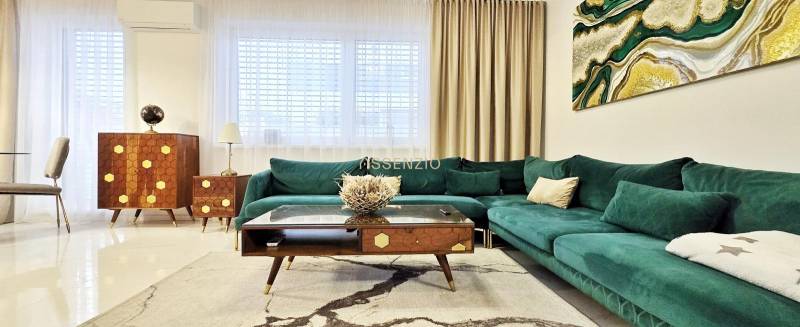 Családi ház zöld árnyalatú kanapéval, fa bútorokkal és művészettel a falon.