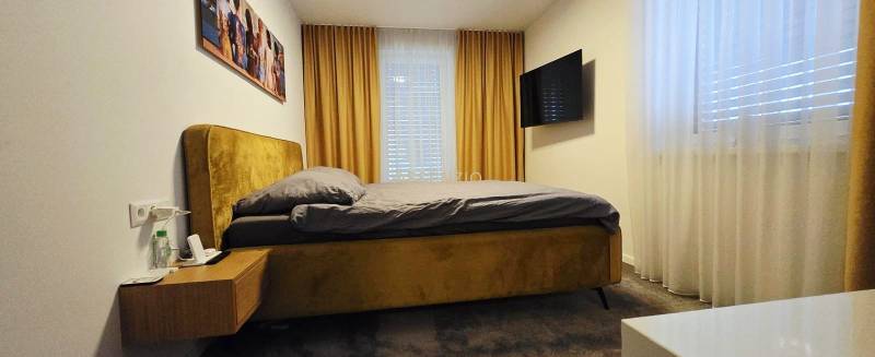 Hálószoba családi házban ággyal, éjjeliszekrénnyel, TV-vel és függönyökkel.