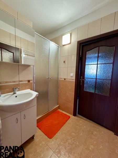 Fürdőszoba zuhanyzóval és mosdóval egy háromszobás lakásban, csempék és tükör.