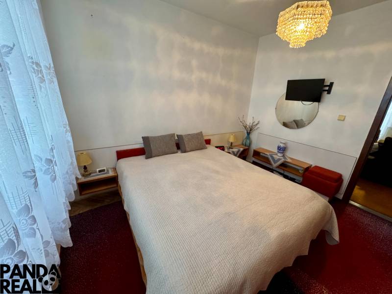 Hálószoba egy háromszobás lakásban ággyal, csillárral és a falon lévő televízióval.