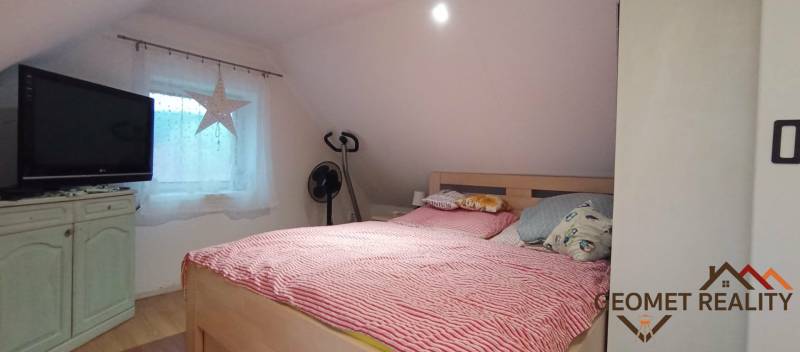 Tetőtéri hálószoba családi házban, ággyal, televízióval és fa dekorációjú padlóval.