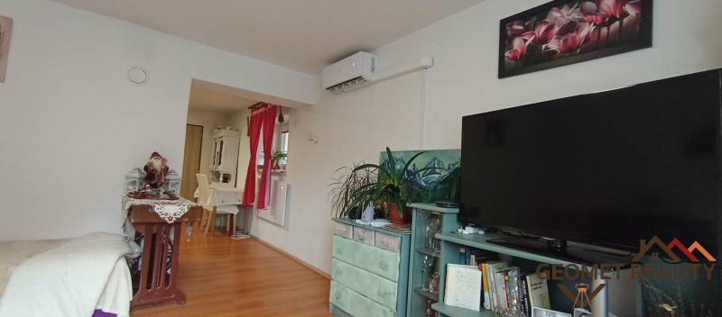 Nappali szoba fa dekoros padlóval, televízióval, légkondicionálóval és dekorációs elemekkel.