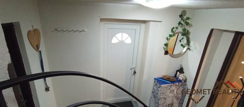 Családi ház bejárata fehér ajtókkal, tükörrel és dekoratív elemekkel.