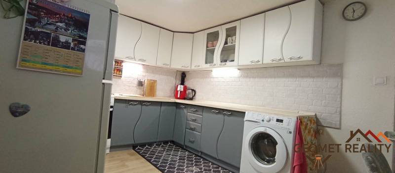 Konyha családi házban fehér és szürke szekrényekkel, fa hatású padlóval.