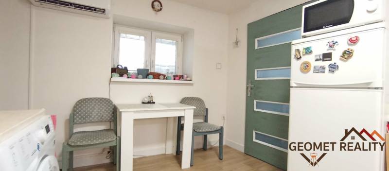 Ebédlő egy családi házban fehér asztallal, hűtőszekrénnyel és fa mintázatú padlóval.