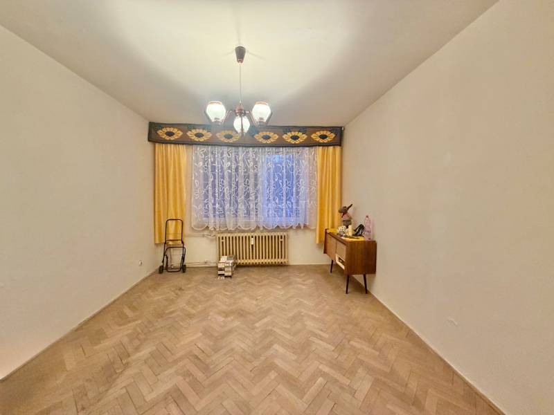 Szoba egy háromszobás lakásban fa dekoros padlóval, függönyökkel és komóddal.