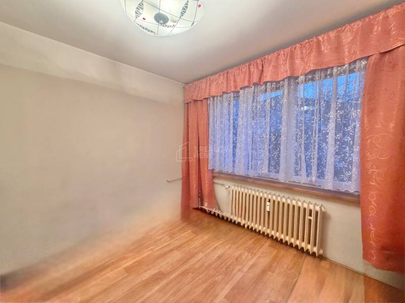 Szoba egy háromszobás lakásban fa dekor padlóval és függönyökkel.