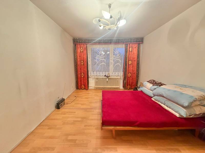 Hálószoba egy háromszobás lakásban ággyal, fa dekorációjú padlóval és világítással.