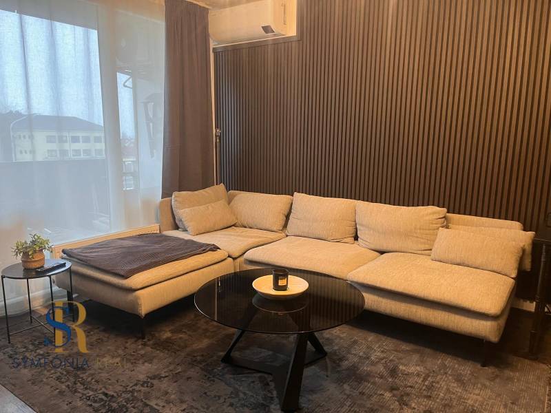 Világos kanapé egy kétszobás lakásban fa dekorációval a falon és asztallal.