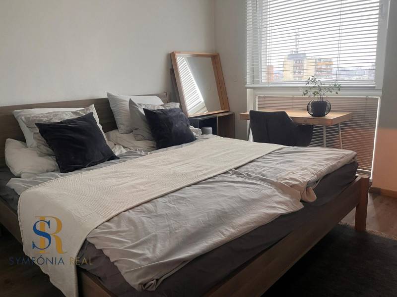 Hálószoba egy kétszobás lakásban ággyal, íróasztallal és fa mintázatú padlóval.