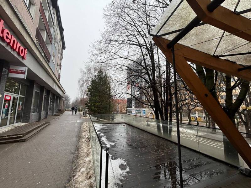 Üzlethelyiségek Poprádon, üvegkorláttal és nedves csempével szomszédos, havas járda.