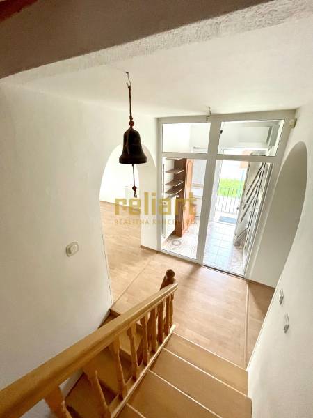 Lépcsőház fa mintás padlóval, bejárati ajtó és csengő családi házban.