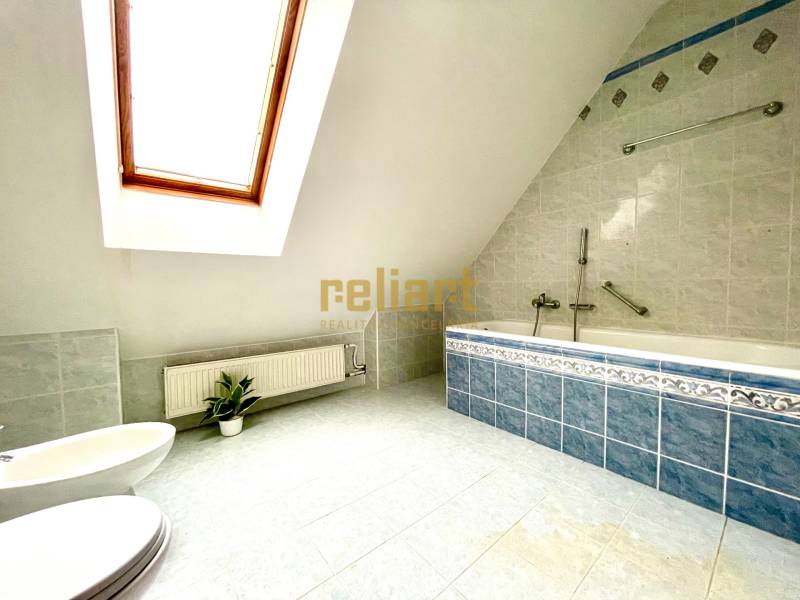 Tetőtéri fürdőszoba sarokkáddal és tetőablakkal egy családi házban.