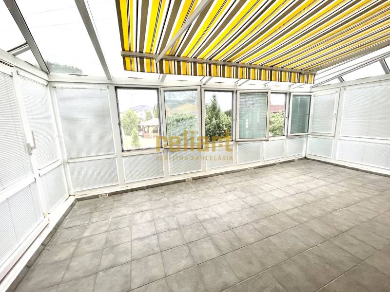 Téli kert egy családi házban nagy ablakokkal és sárga csíkos rolókkal.