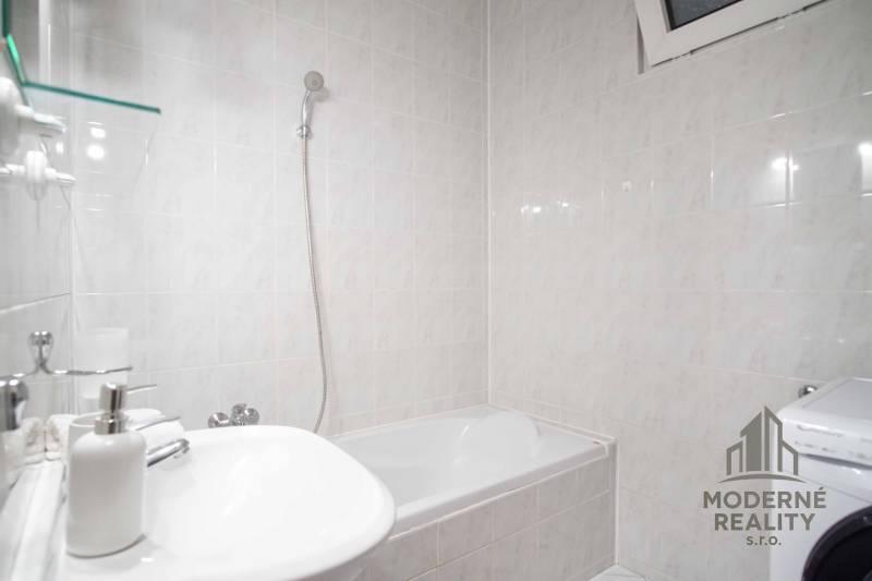 Fürdőszoba káddal és mosógéppel egy 4 szobás lakásban. A falakat világos csempék borítják.