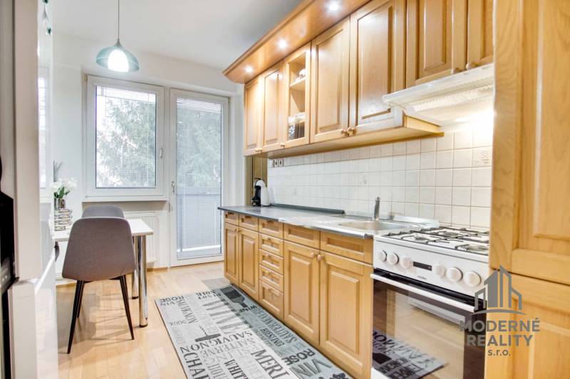 Konyha egy 4 szobás lakásban fa mintázatú padlóval és étkezőasztallal.