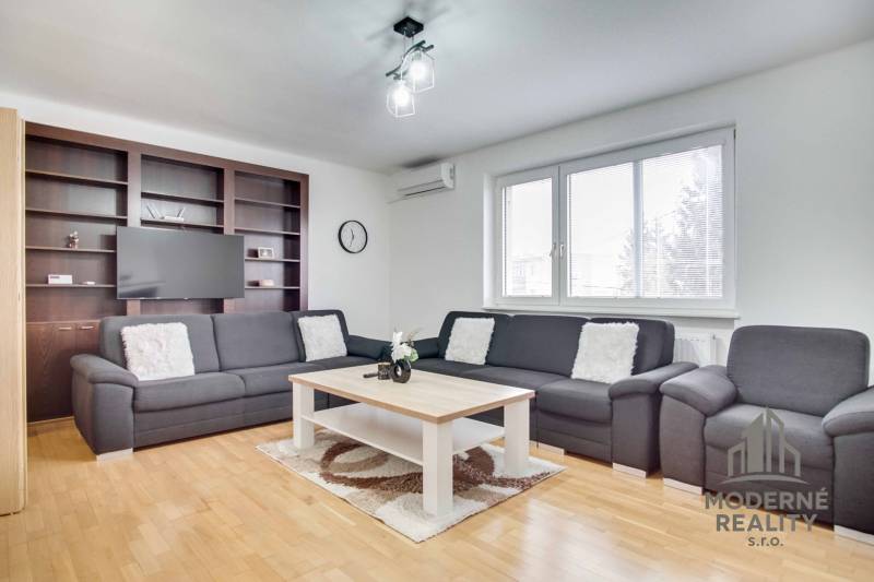 Nappali egy négy szobás lakásban kanapéval, dohányzóasztallal és fa mintázatú padlóval.