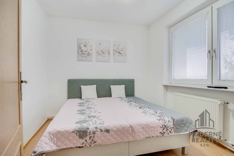 Hálószoba világos ággyal, fa dekoros padlóval és díszes képekkel a 4 szobás lakásban.