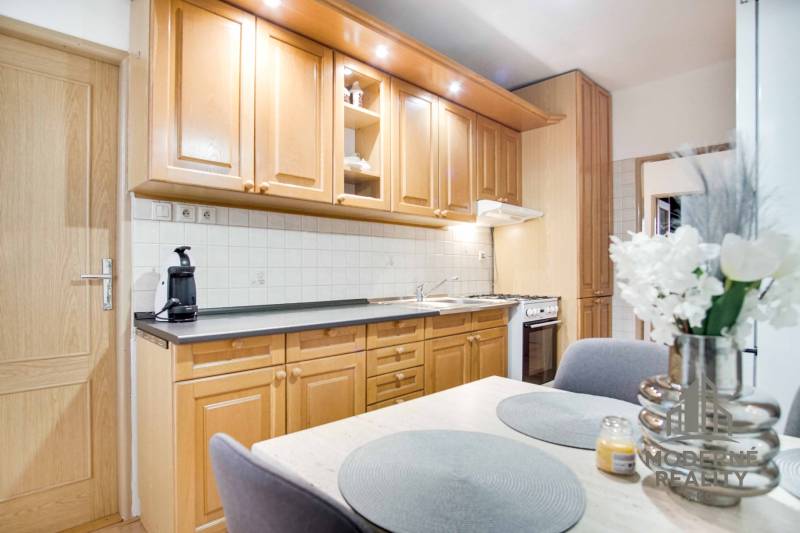 Konyha egy 4 szobás lakásban fa szekrényekkel, virágokkal és étkezőasztallal.