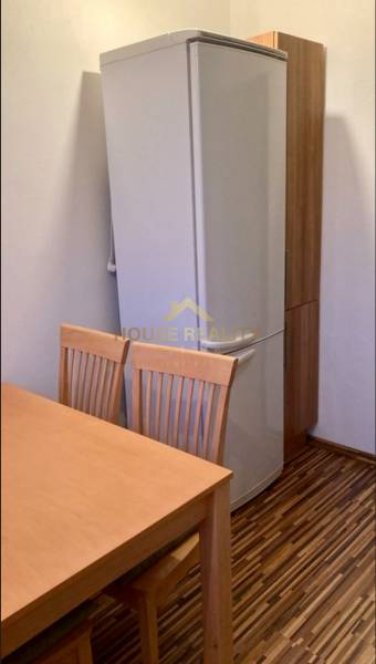 Konyha egy háromszobás lakásban hűtőszekrénnyel, fa asztallal és székekkel, fapadló dekorációval.