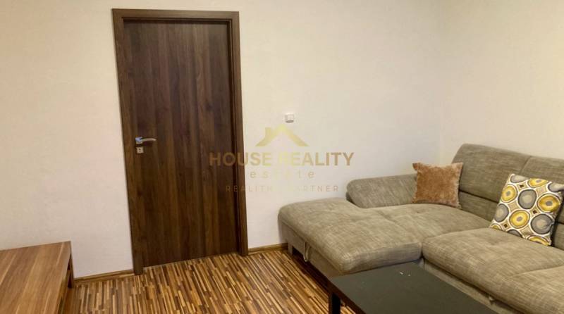 Nappali kanapéval, fa dekor padlóval és sötét ajtókkal egy háromszobás lakásban.