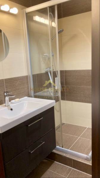 Fürdőszoba mosdóval, zuhanyzóval és barna falburkolatokkal egy háromszobás lakásban.