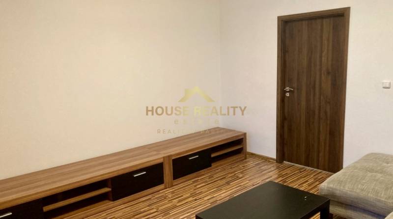 Nappali szoba fa mintás padlóval egy háromszobás lakásban, világos falak, fa bútorok.