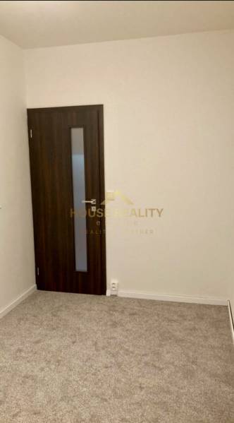 Szoba egy háromszobás lakásban szőnyegpadlóval és sötét ajtókkal.