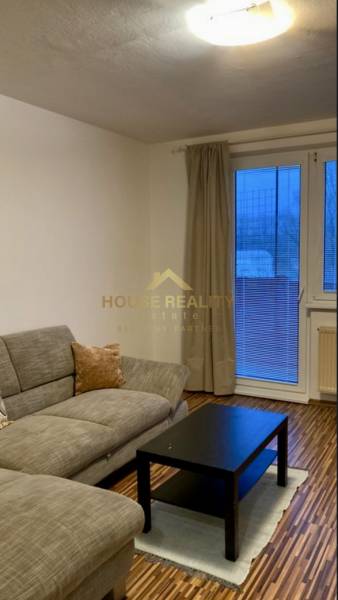 Nappali kanapéval, fekete asztallal és fa dekorációjú padlóval egy háromszobás lakásban.