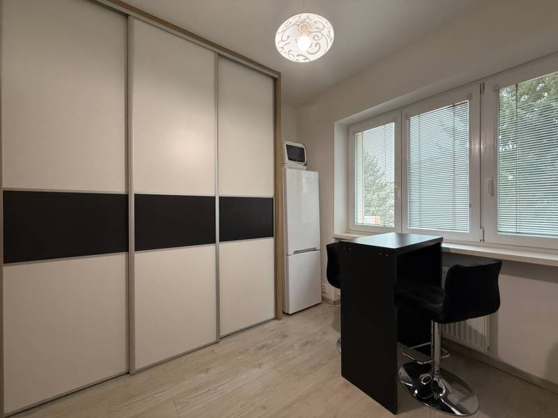 Egyszobás lakás berendezése, tolóajtós szekrény, magas hűtőszekrény, asztal két székkel.