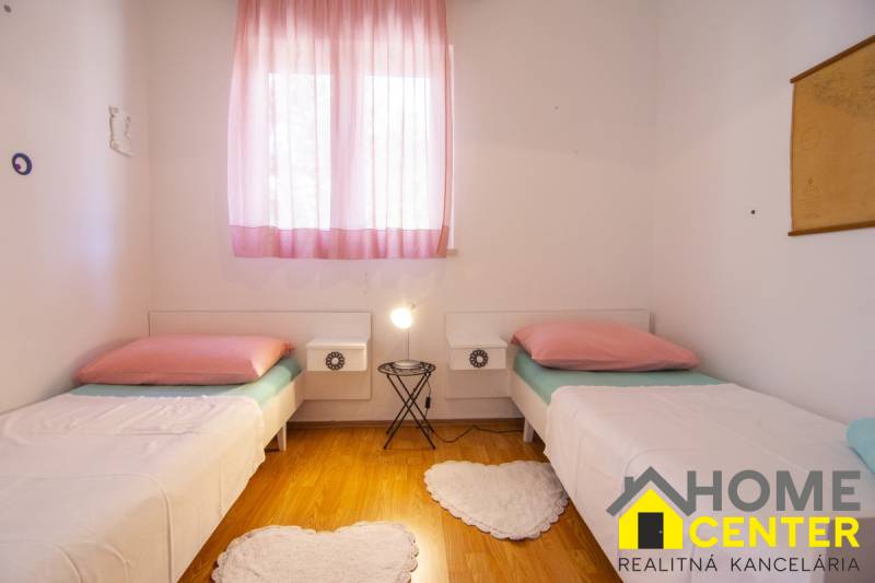 Világos hálószoba két ággyal, rózsaszín függönyökkel és fa dekorációjú padlóval.