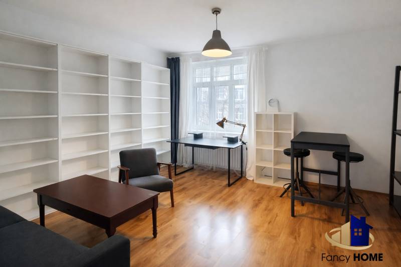 2 szobás lakás belső tere fa hatású padlóval, nagy polcokkal és modern bútorokkal.