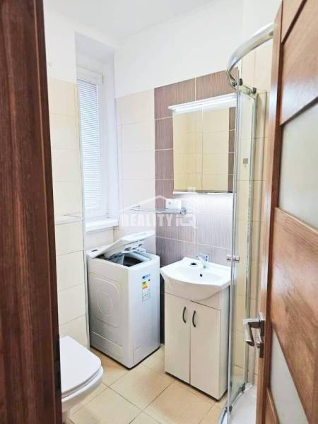 Fürdőszoba a garzonlakásban mosógéppel, zuhanyzóval és mosdóval.