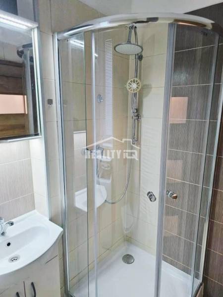 Fürdőszoba üveg zuhanykabinnal és világos csempékkel a garzonlakásban.