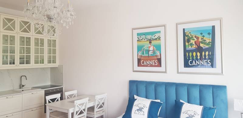 Egy szobás lakás belső tere konyhával, csillárral és képekkel a kék ágy felett.