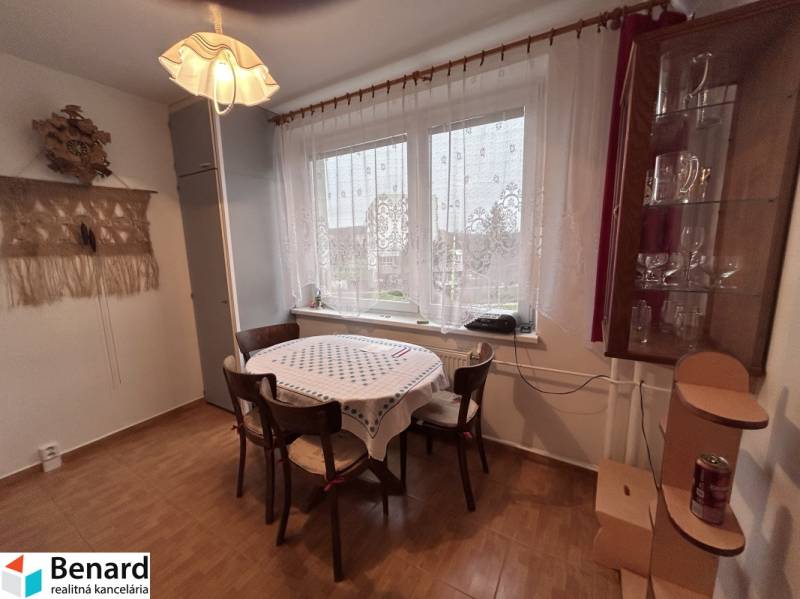 Étkező sarok egy kétszobás lakásban fa mintázatú padlóval, asztallal, székekkel, függönyökkel.