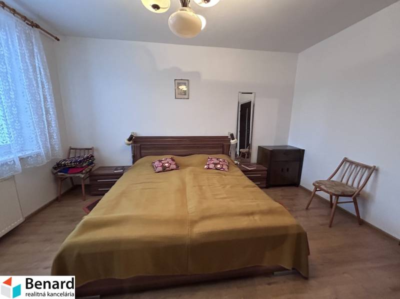 Hálószoba egy kétszobás lakásban ággyal, székekkel és fa dekorációjú padlóval.