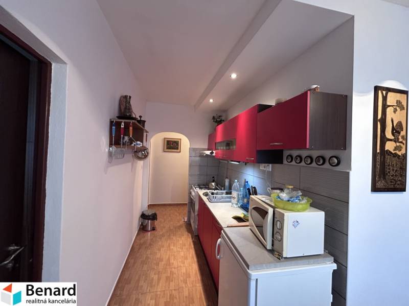 Konyha piros szekrényekkel és fa dekoros padlóval egy kétszobás lakásban.