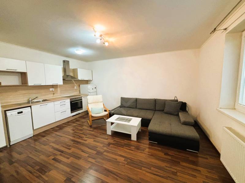 Nappali egy kétszobás lakásban sarokkanapéval és konyhabútorral.