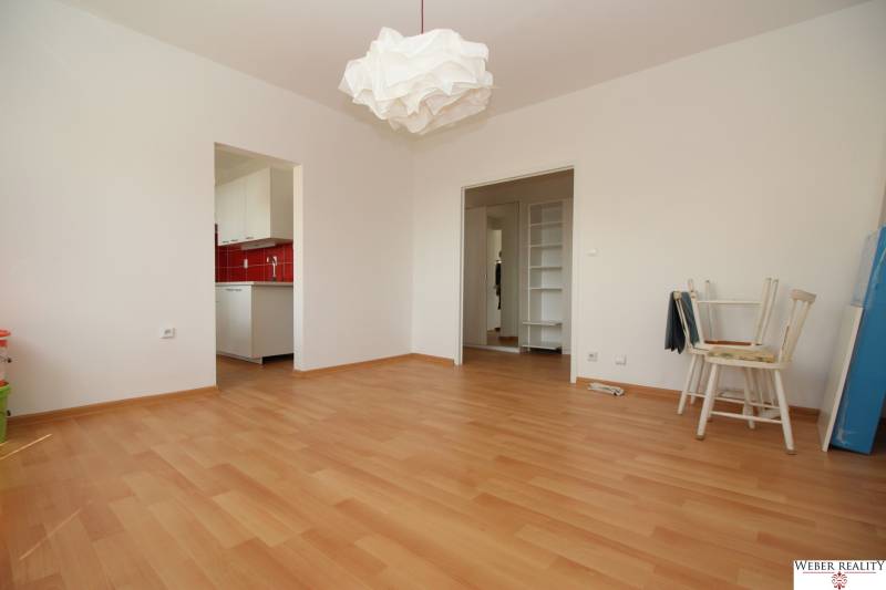 Szoba fa mintázatú padlóval, fehér bútorokkal és piros konyhai fallal.