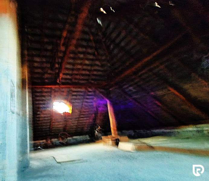 Családi ház tetőtéri szobája fa gerendákkal és ablakkal.