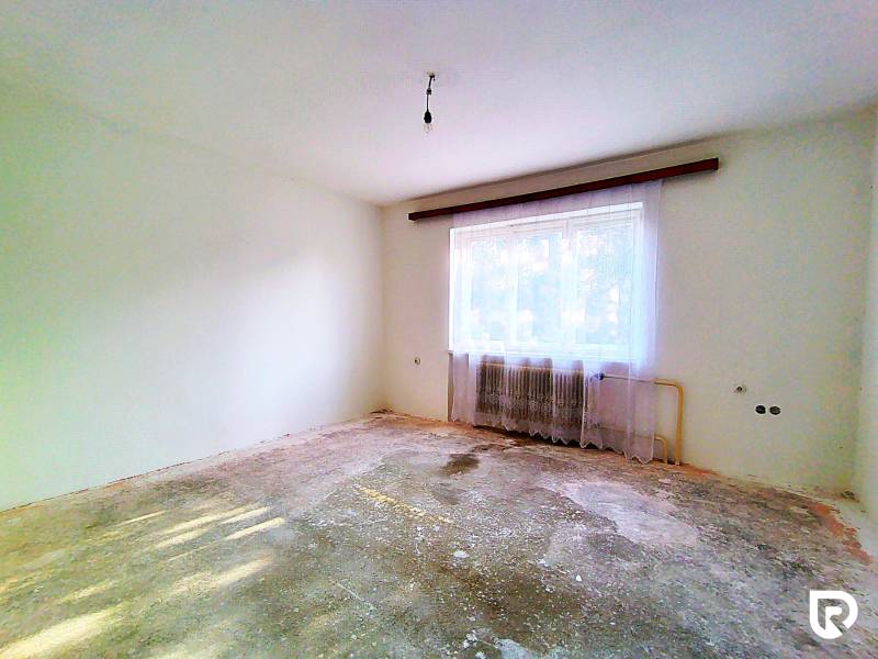 Üres szoba egy családi házban, kopott padlóval, radiátorral és függönyökkel.