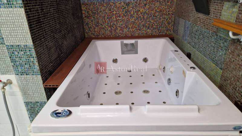 A családi ház fürdőszobájában egy nagy hidromasszázs kád található, színes mozaik csempével díszítve.